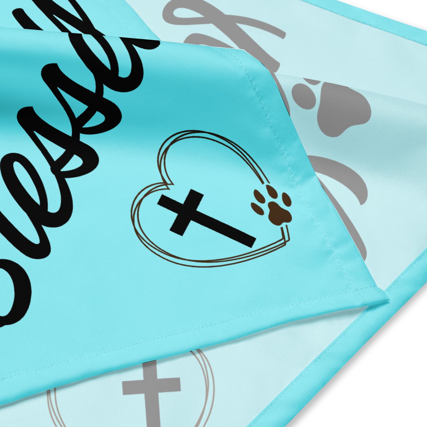 Aqua fabric showing both the front and backside of the bandana and part of the artwork on both sides. You can see a heart, a pawprint, a cross, and part of the words.