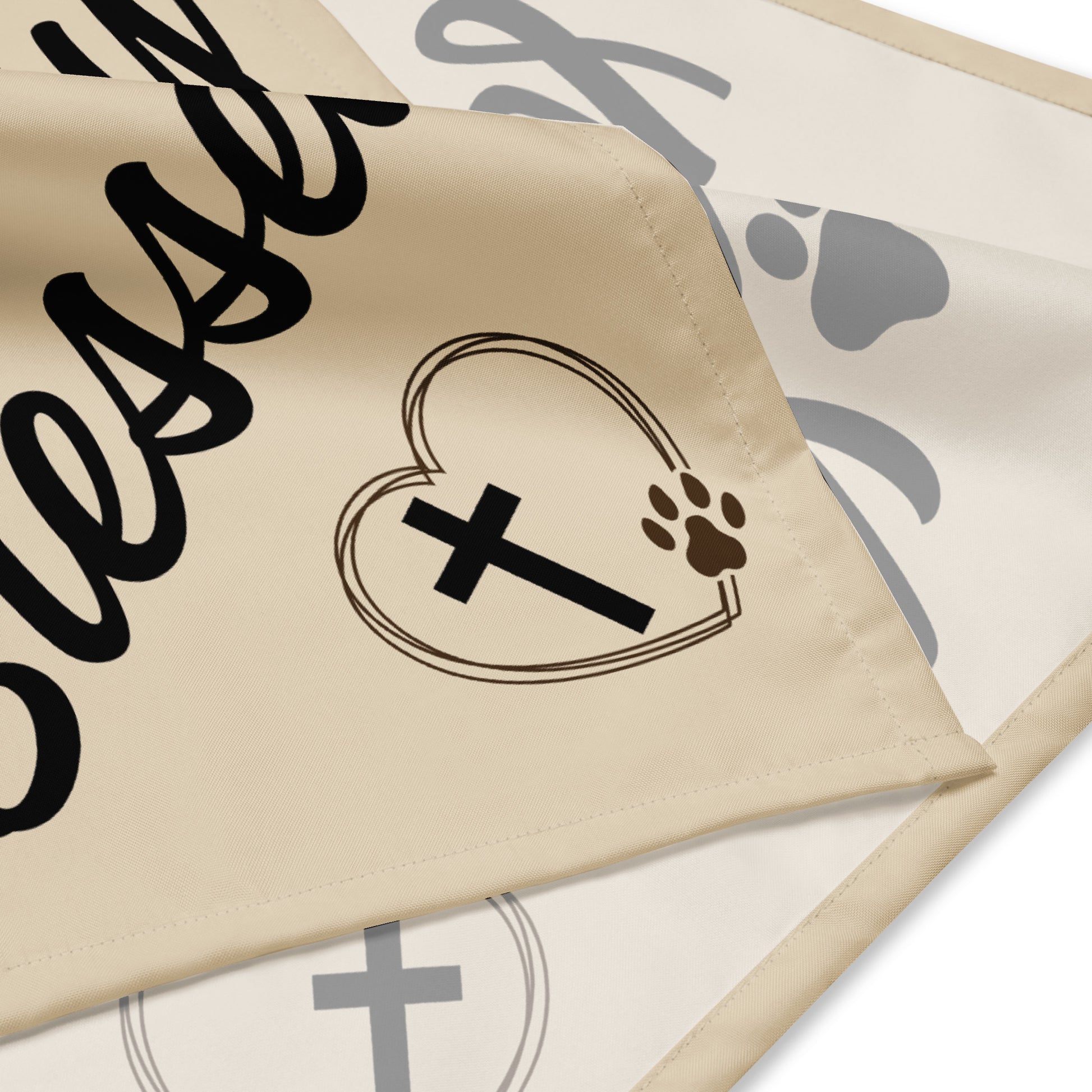 Corners of a tan bandana show the hem and front and back sides with part of the design on it. A heart outline, thick cross, paw print, and some text are visible.