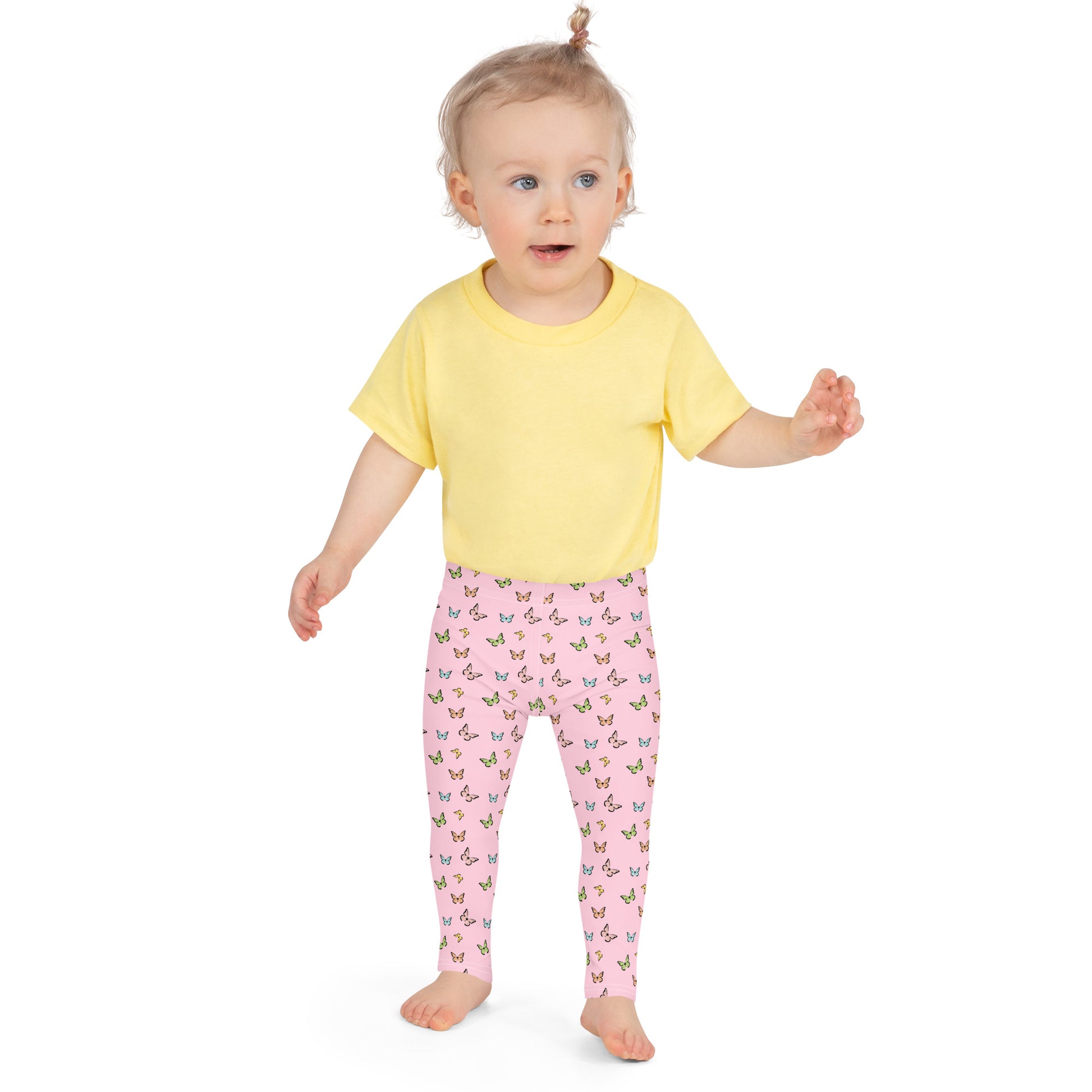 Toddler girl with bare feet standing, with tiny ponytail wearing yellow short-sleeved t-shirt and pink leggings with butterflies all over them. 