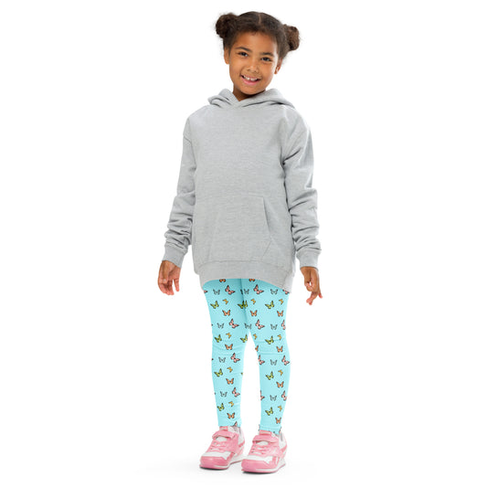 Smiling little girl with dark hair standing, wearing light gray sweatshirt, aqua leggings with pastel butterflies, and pink and white tennis shoes.