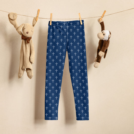 A clothesline with a stuffed rabbit hanging on the left with a clothespin by one ear, a pair of navy leggings with an all-over white ornate cross print hanging by two clothespins in the center, and a stuffed monkey pinned with a clothespin by one arm on the right.