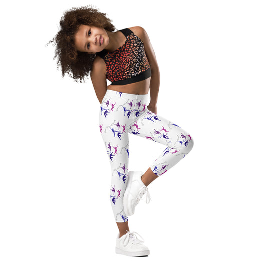 A young girl with dark curly hair, in a stretching pose , wearing a dark print short dance or exercise top, white athletic shoes, and a pair of white leggings with pink and purple dancers in different poses all over them.