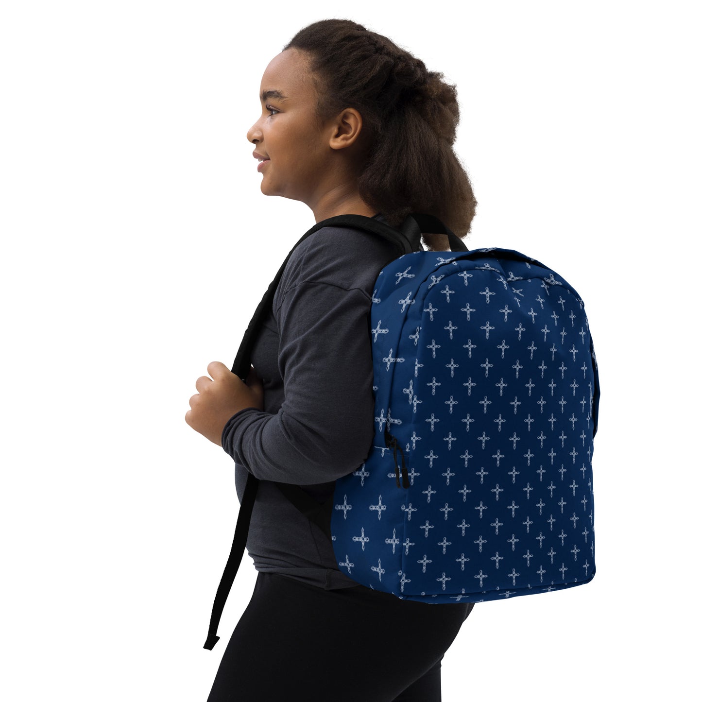 Dark-haired pre-teen girl dressed in dark clothes with navy blue backpack with ornate white cross print on it slung over her left shoulder.