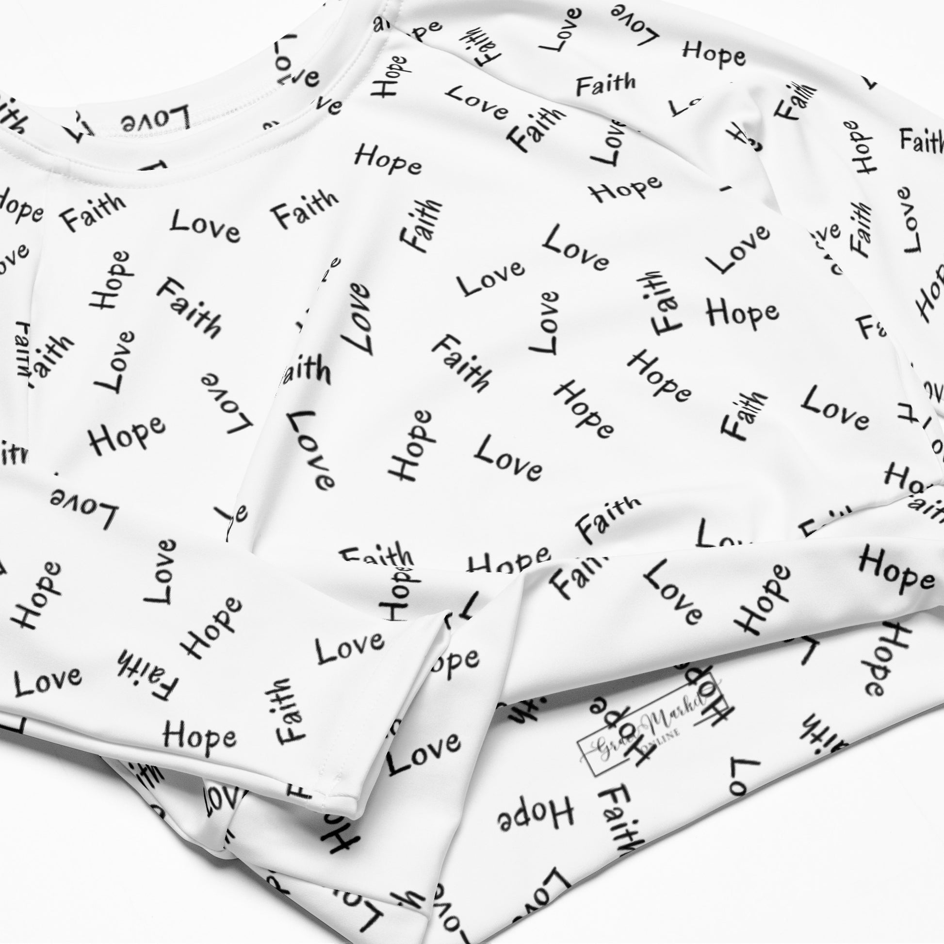 A shirt folded on a white background showing up close the all-over Faith Hope Love print and also the inside printed brand label for Grace Market Online.