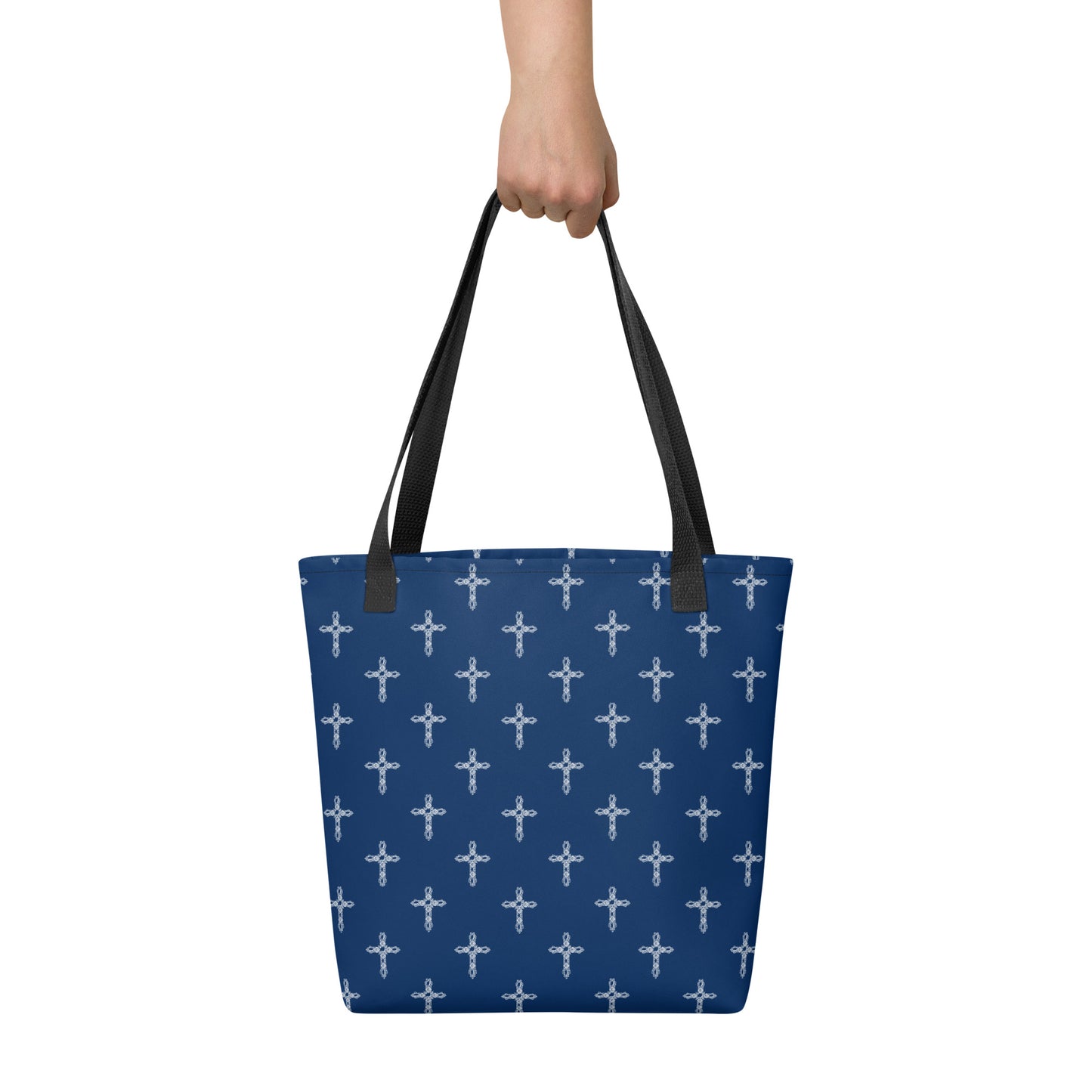 Human hand holding black handles on a navy blue tote bag with white crosses on it.