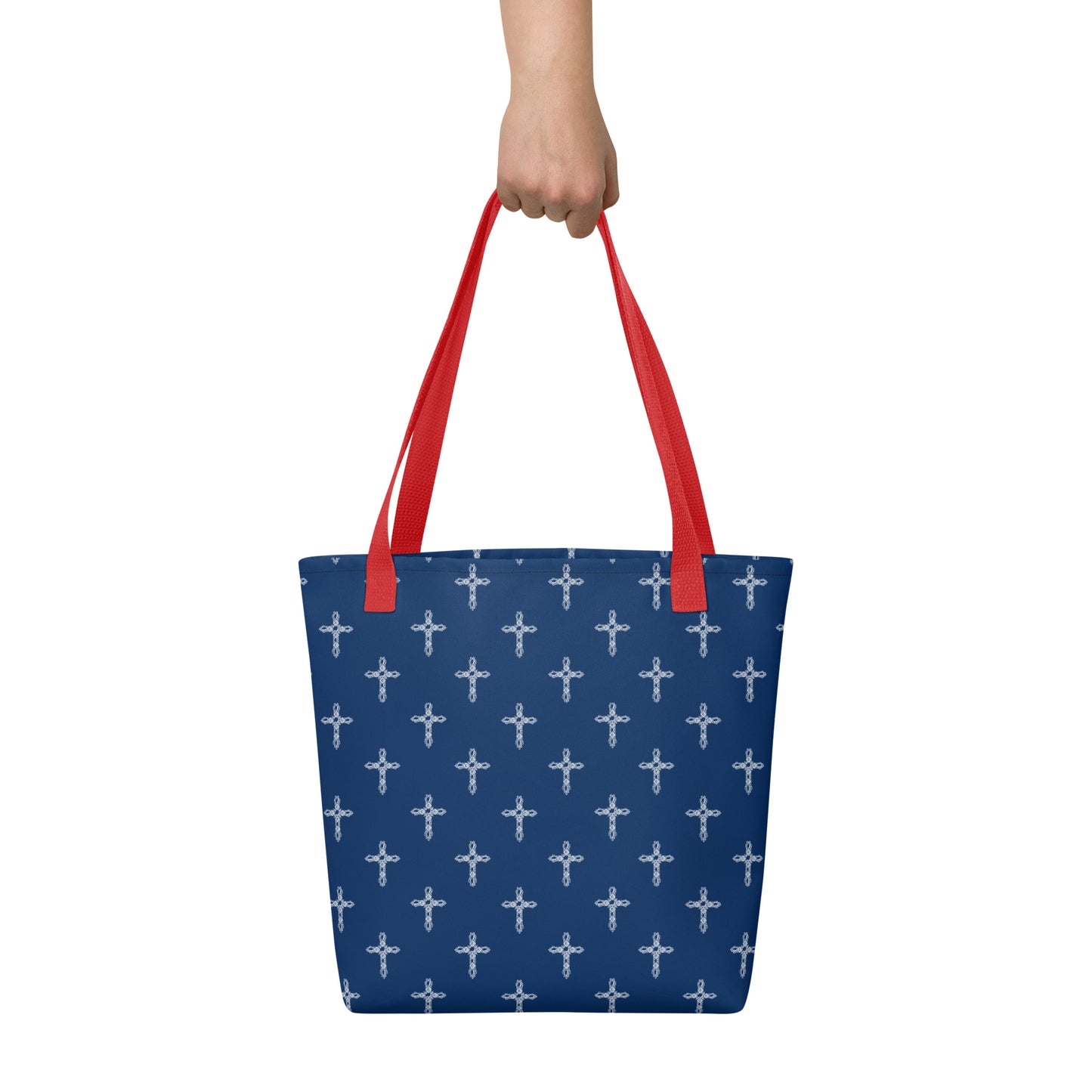 A woman's hand holds the red straps of a navy blue purse or bag that has a pattern of ornate white crosses on it, all against a solid white background.