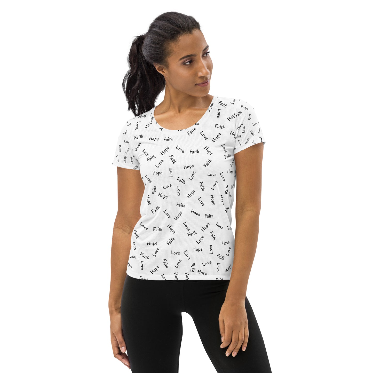 Woman with long dark hair in a pony tail is wearing black leggings and a white, short-sleeve t-shirt in an all-over Faith Hope and Love print.