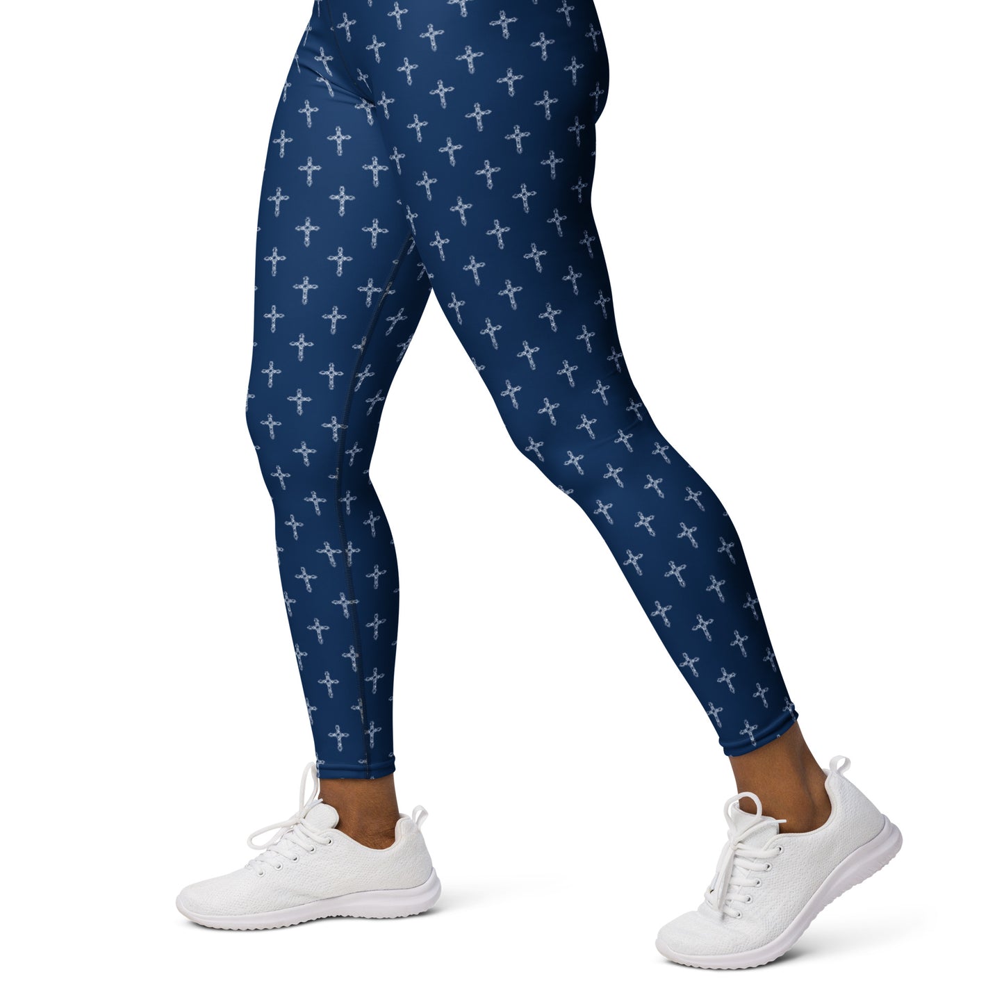 A woman's body from the waist down against a solid white background and she's wearing white canvas athletic shoes and navy blue leggings with an ornate cross pattern all over them.