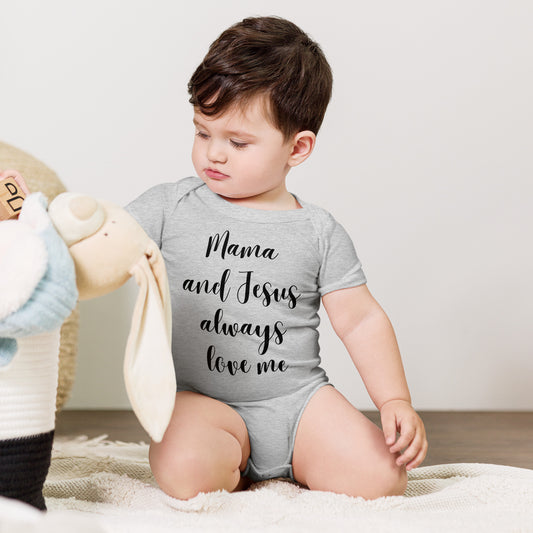 A dark haired toddler boy kneels on a blanket or rug playing with a stuffed bunny and he is wearing a light gray onesie that says Mama and Jesus always love me.