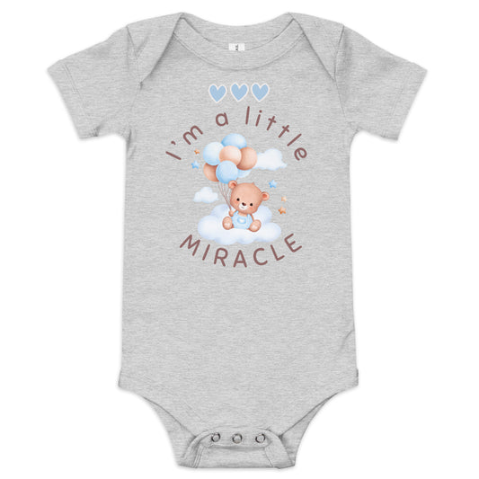 Gray short-sleeved onesie with a teddy bear in blue overalls holding blue and brown balloons that says "I'm a little MIRACLE" with three little blue hearts above it.