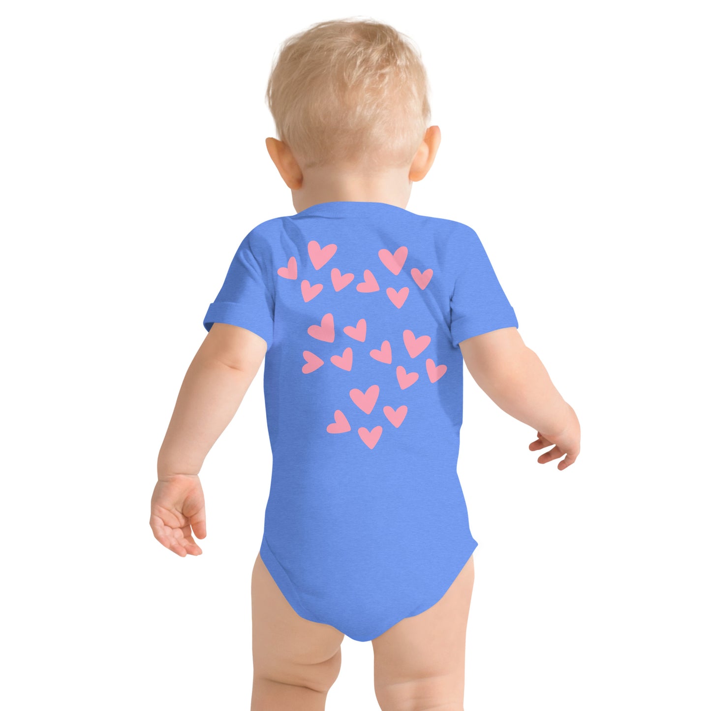 Light pink hearts of varying sizes cover the back portion of a blue short-sleeved onesie on a blonde-haired child who is walking away. 