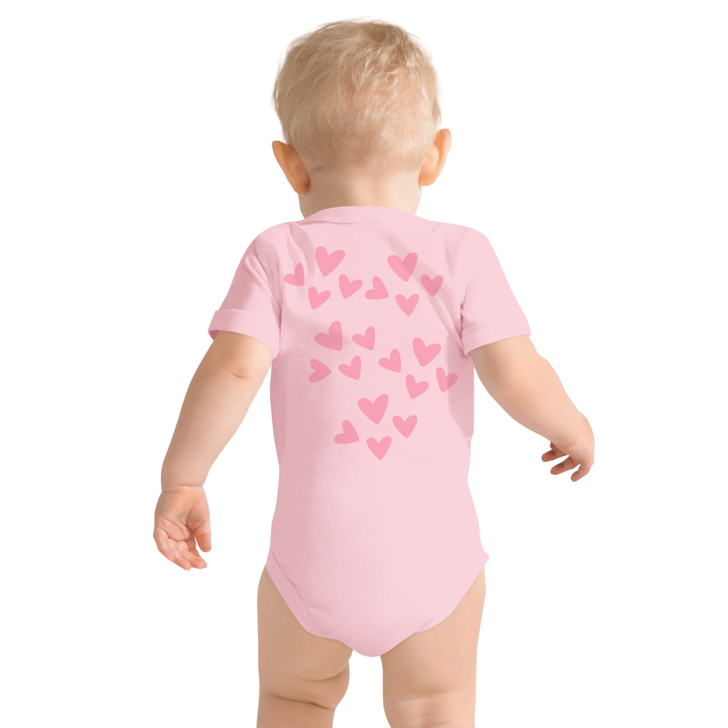 Pink hearts of varying sizes stand out as a darker pink on a lighter pink short-sleeved onesie being worn by a toddler. We see the back of the toddler and the onesie.