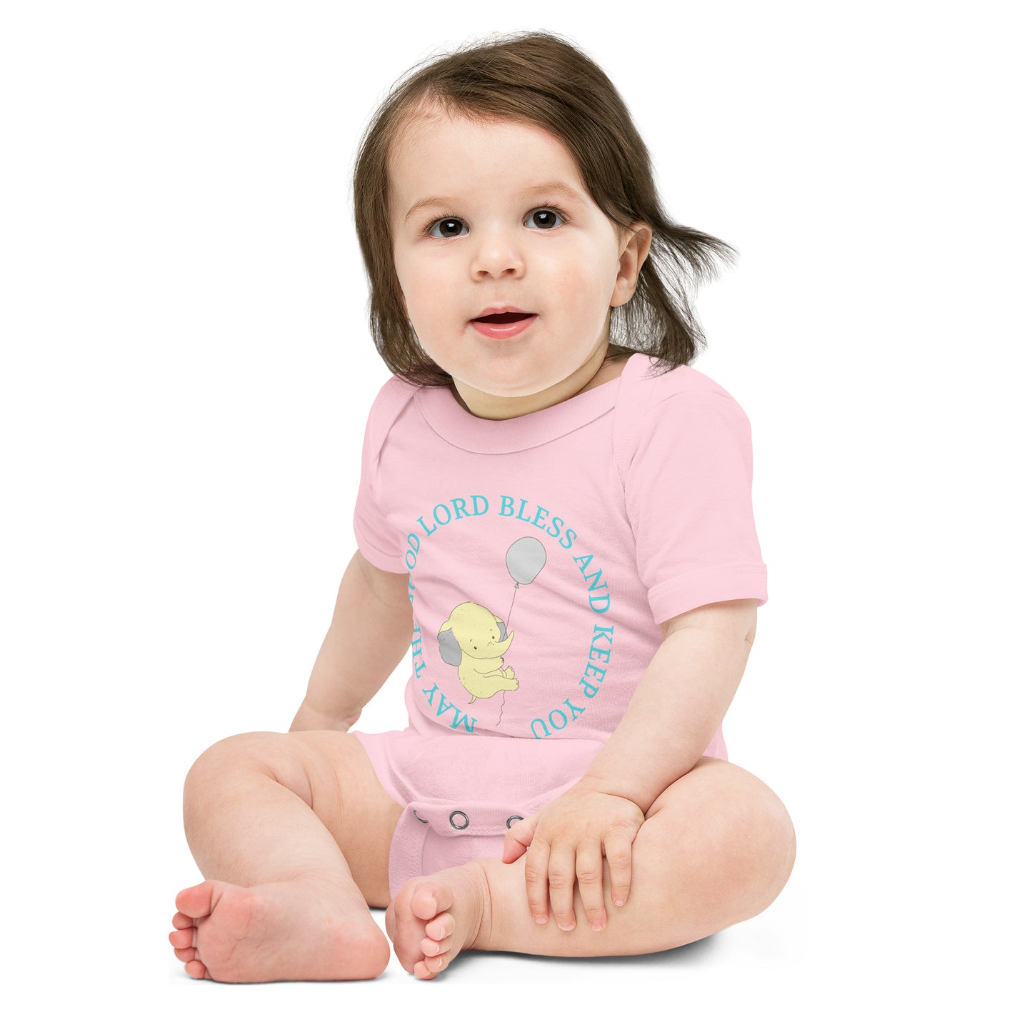 A toddler is sitting on a plain white background wearing a pink onesie with aqua words on it and a yellow elephant holding a balloon that is floating away.