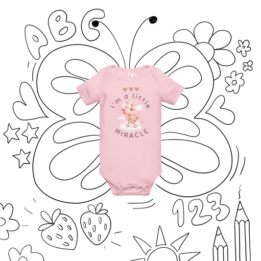 Pink short-sleeved onesie with a teddy bear in pink overalls on a cloud holding pink and brown balloons and with three pink hearts that says I'm a little MIRCLE on the front is in the center of a white background with doodling on it so that it looks like butterfly wings were drawn around it and the onesie is the butterfly body, and some other little kid-friendly doodles.