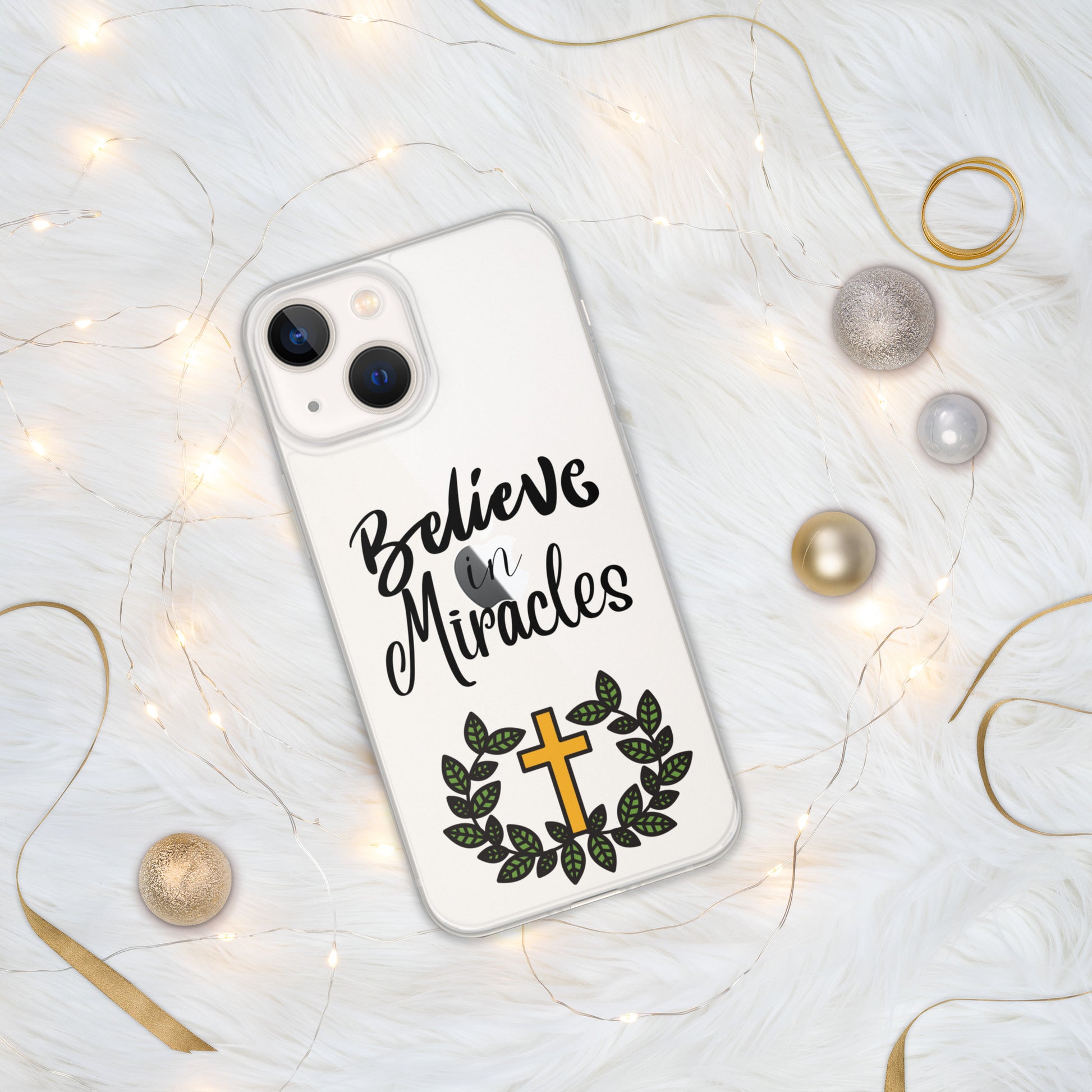 iPhone case reads:  Believe in Miracles and also a gold cross surrounded by green leaves. Then the phone is on a white background with curly gold ribbons, tiny white lights, and silver and gold balls around it.