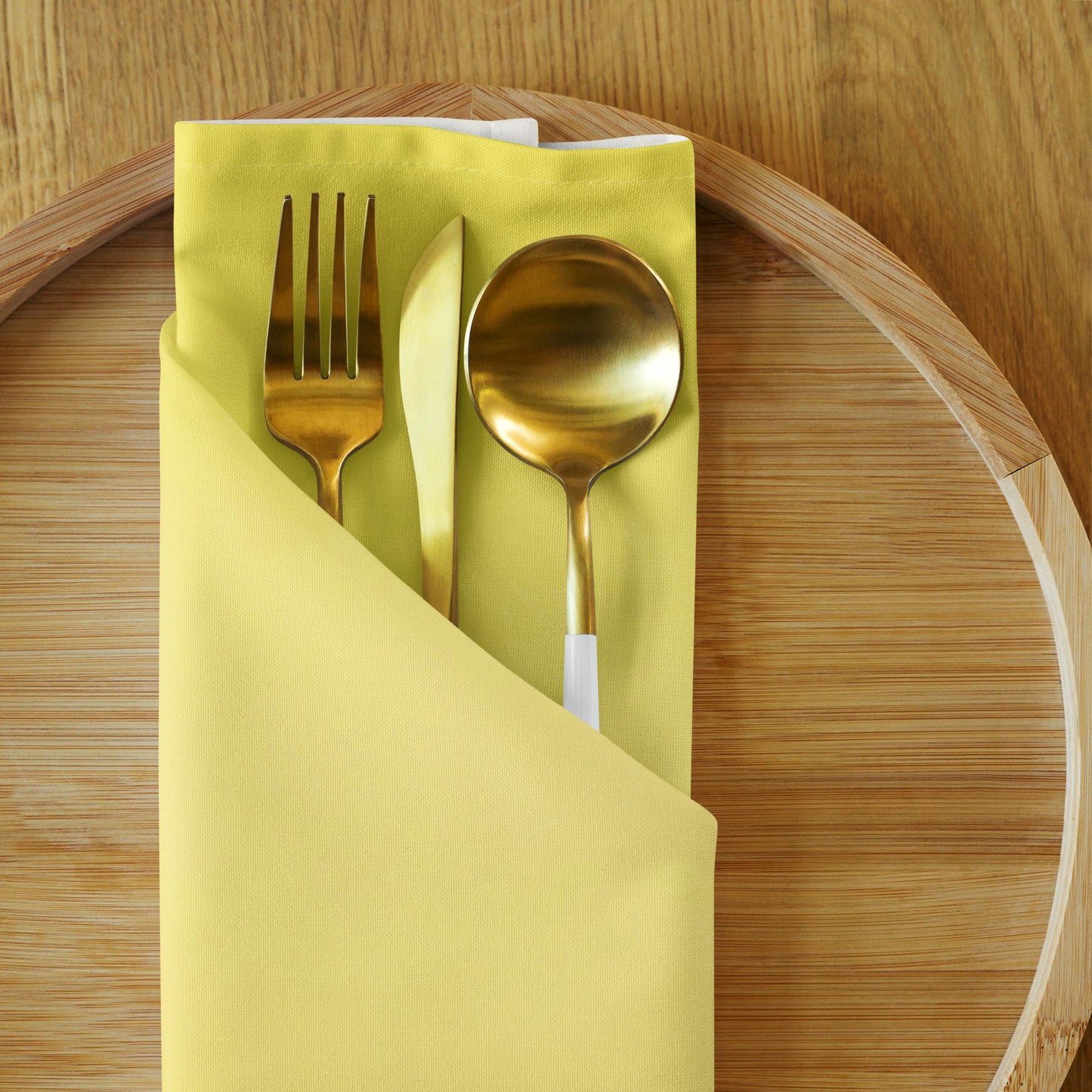 Yellow cloth napkin folded with utensils  tucked into it on wooden charger