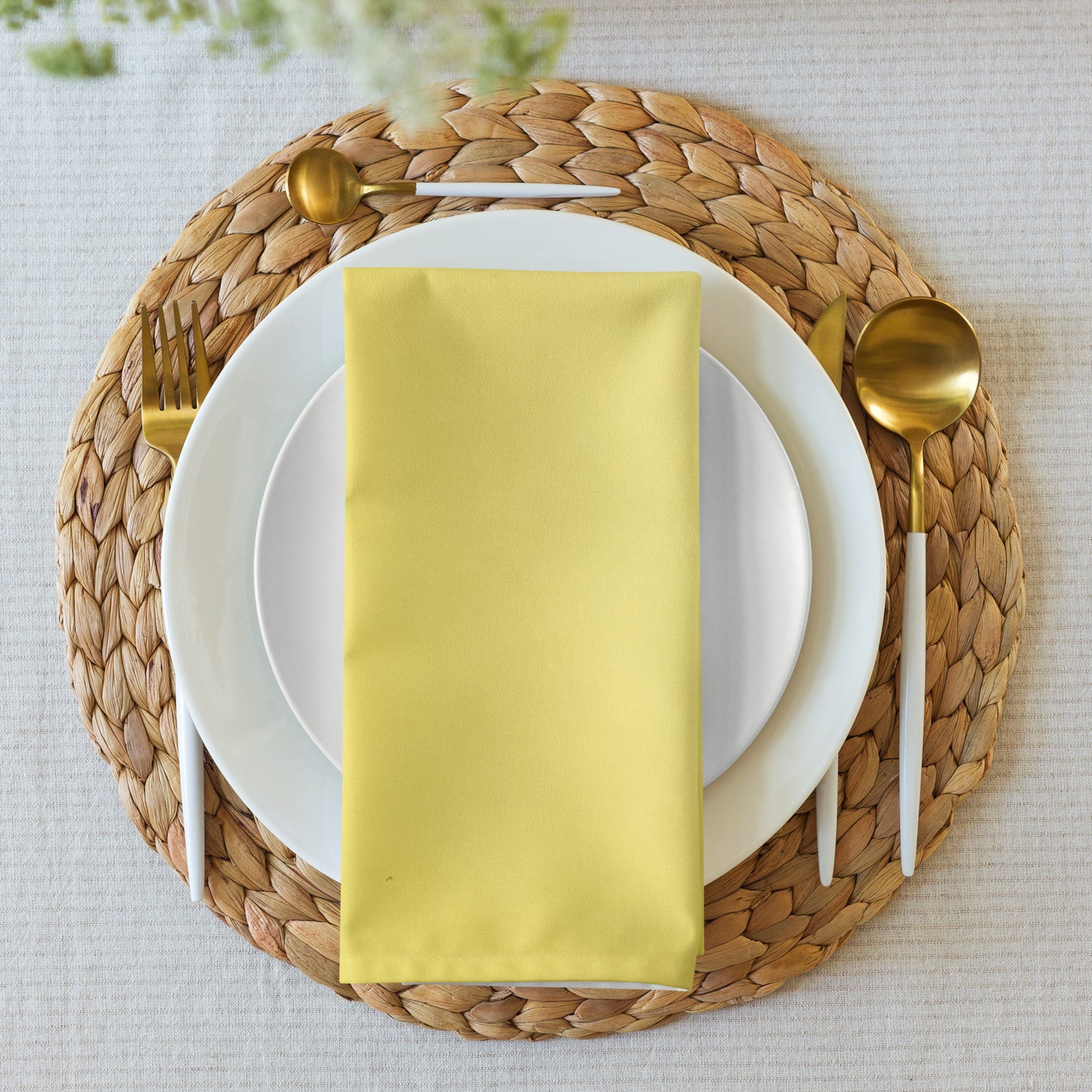 Yellow cloth napkin folded and placed in center of dinner place setting on rattan placemat.