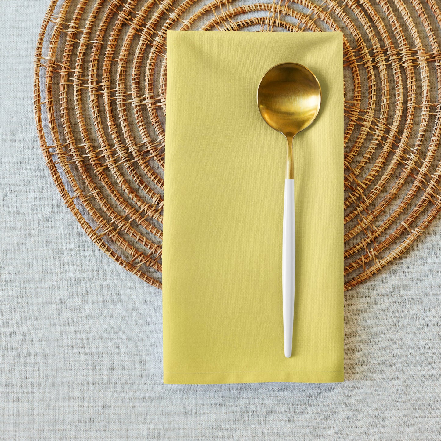 Yellow cloth napkin with gold spoon placed on it, sitting on round placemat.