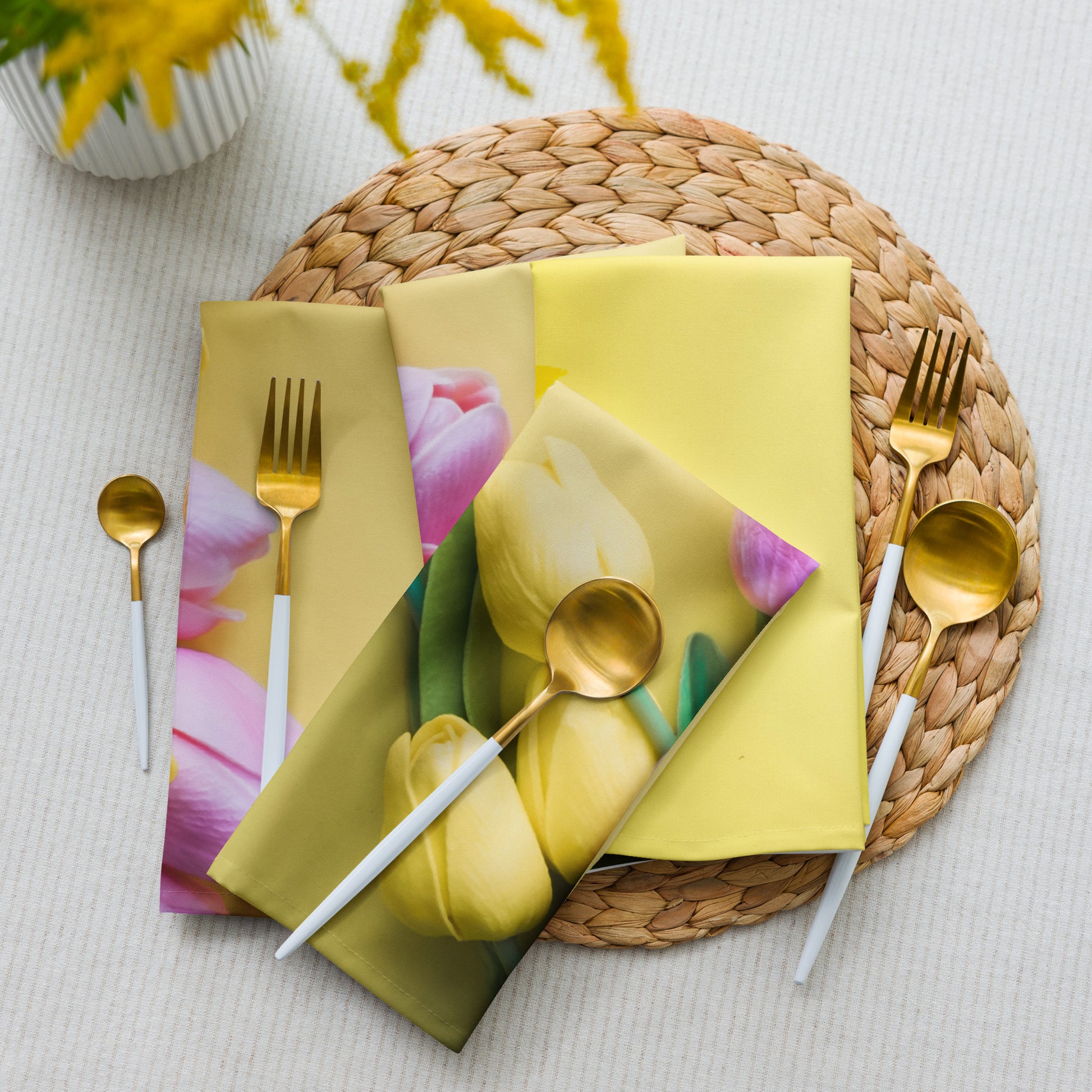 Yellow tulips on cloth napkins with utensils on a woven placemat on a table.