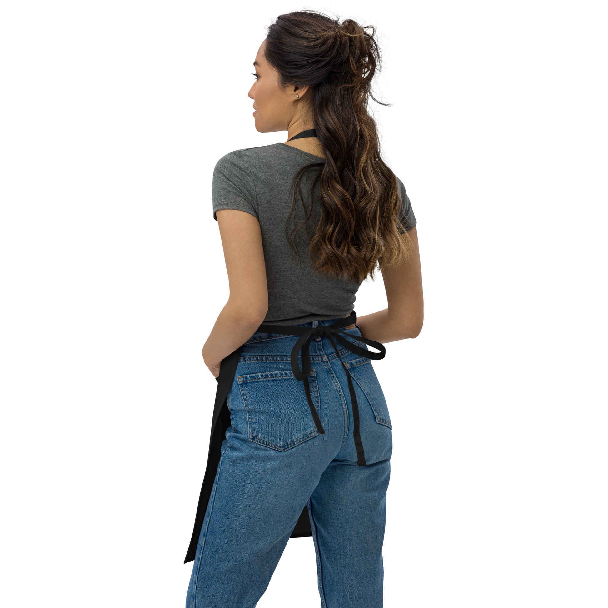 Back view of woman with long medium dark hair wearing blue jeans, short-sleeve gray t-shirt, and back view of the  black apron ties.