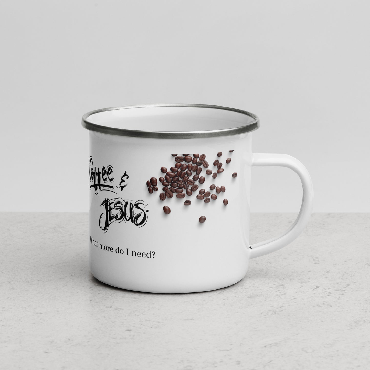 A white metal or enamel coffee mug turned with the handle showing on the right side of the photo and the mug has a picture of coffee beans and the words Coffee & Jesus What more do I need on the side.