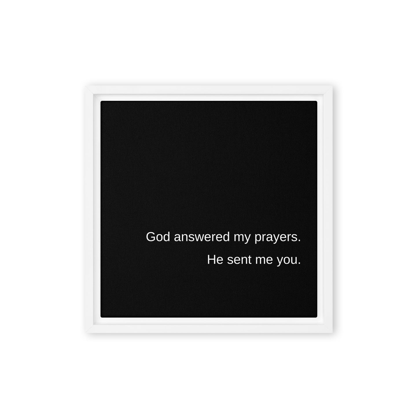 Square black stretched canvas with the words God answered my prayers. He sent me you. on it in white text with a white frame around it, on a white wall.