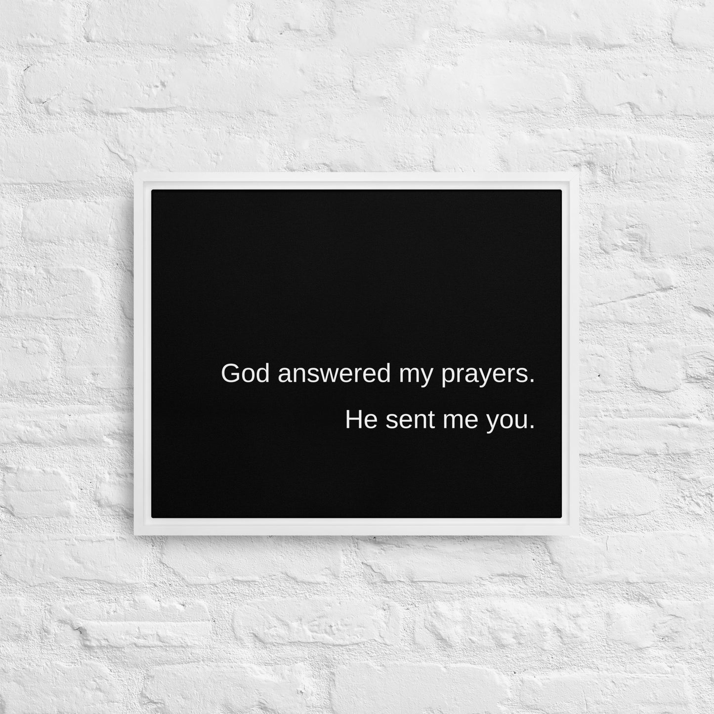 White painted brick wall with white framed black print that says:  God answered my prayers. He sent me you. in plain white text.