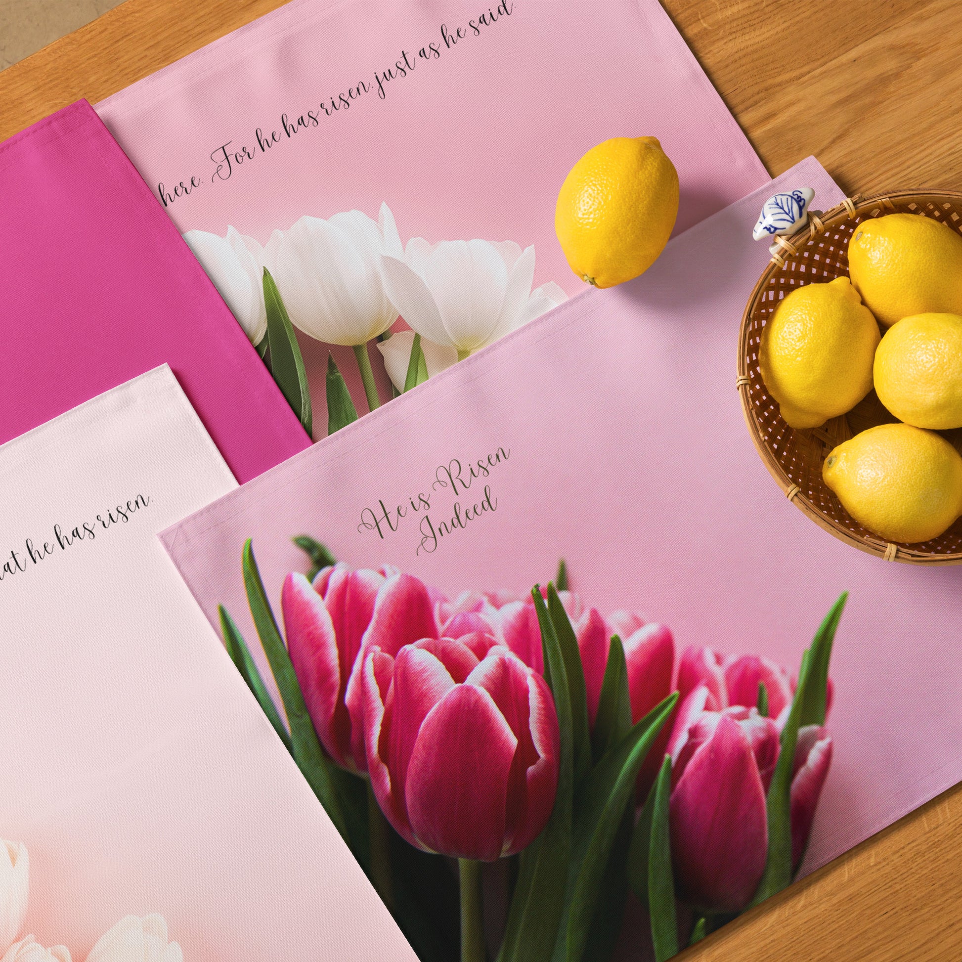 Four different pink fabric placemats with tulips and scripture on them on a table with a bowl of yellow lemons on table.