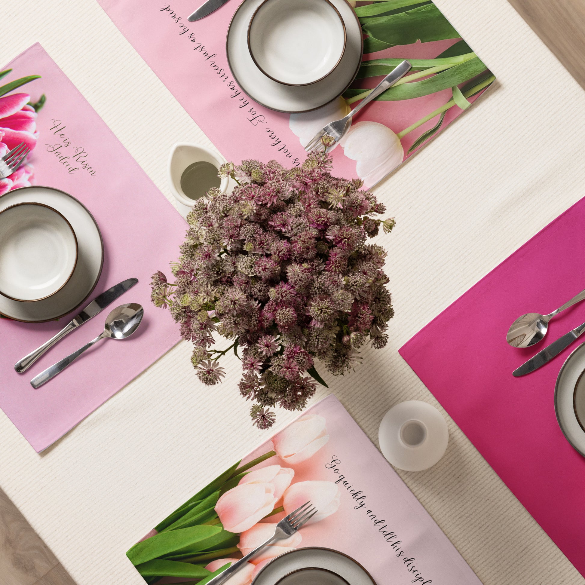 Table set for dinner with four pink fabric tulip placemats, dishes, and silverware, and a vase of flowers in the middle.