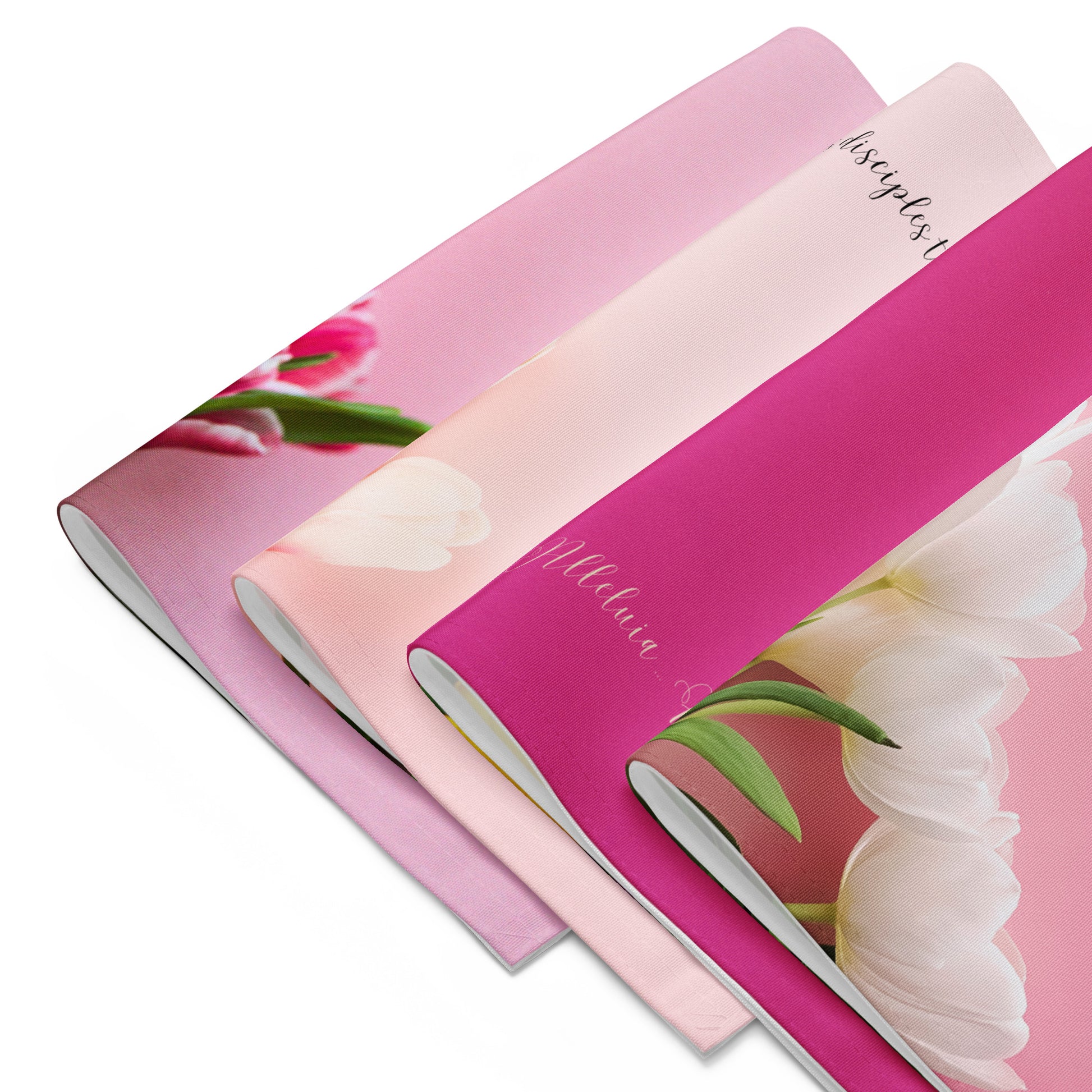 Four different pink fabric placemats with tulips and words on them, all folded in half and stacked in a row.