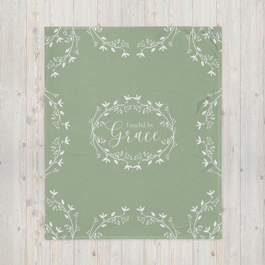 Sage green blanket with Touched by Grace in a white floral wreath in the center