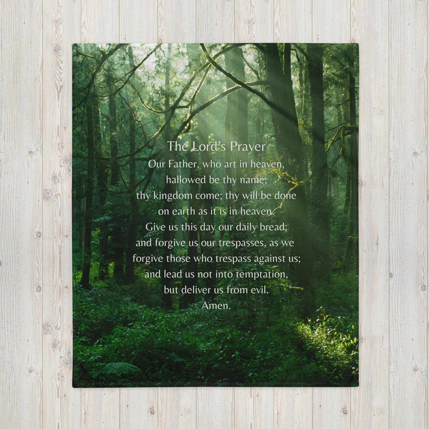 A throw blanket with a picture of a green forest and The Lord's Prayer printed on top of it in white.