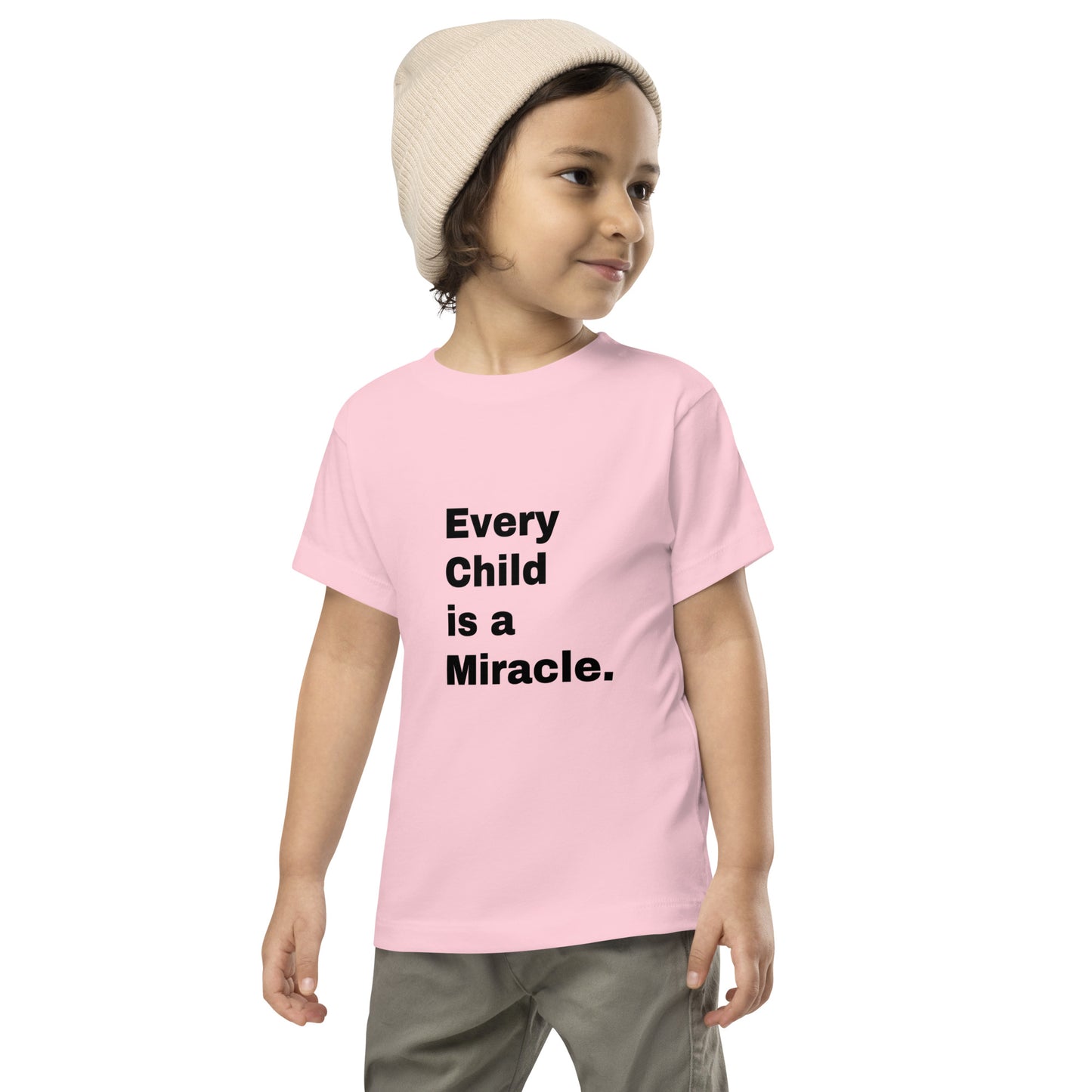 Toddler wearing gray pants and a knit hat and a pink short-sleeve t-shirt with black text that says "Every Child is a Miracle."