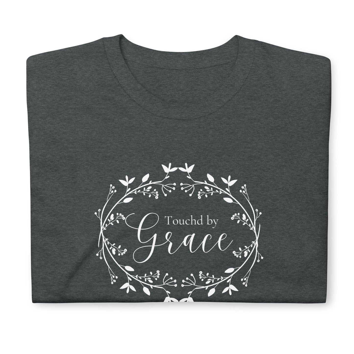 Close up of the top of a folded gray t-shirt and you can see that on the front is a viney kind of wreath with flowers in white and white text that says "Touched by Grace" in two fonts.