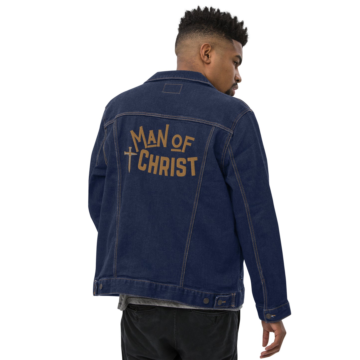 A back view of a man wearing a black denim jacket with the words "Man of Christ" embroidered in big gold letters across the back and a cross made of nails embroidered beside the words.