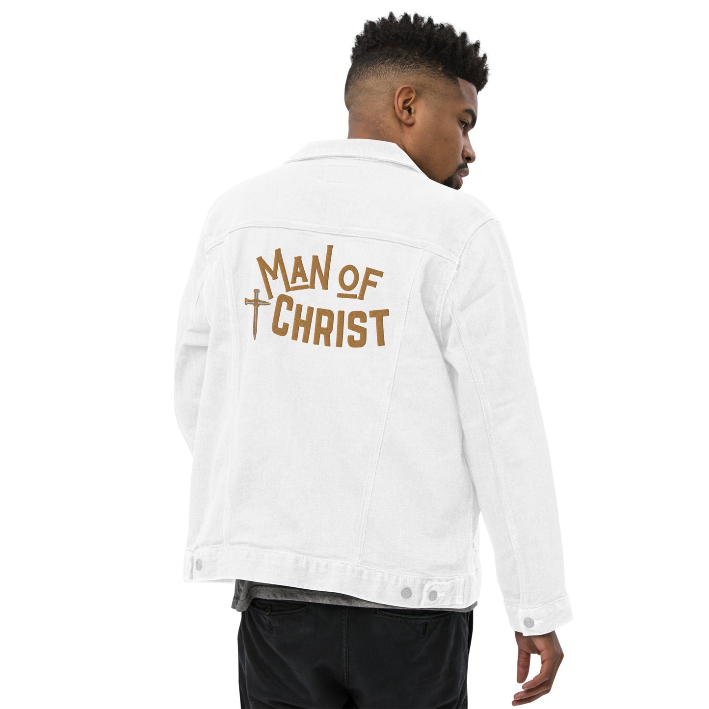 A man wearing a white denim jacket, turned so we can see that the back has a large embroidered design featuring a cross made of nails and the words Man of Christ in gold lettering.