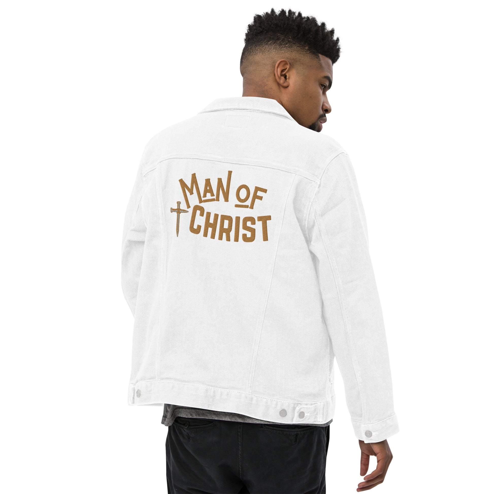 A man wearing a white denim jacket, turned so we can see that the back has a large embroidered design featuring a cross made of nails and the words Man of Christ in gold lettering.