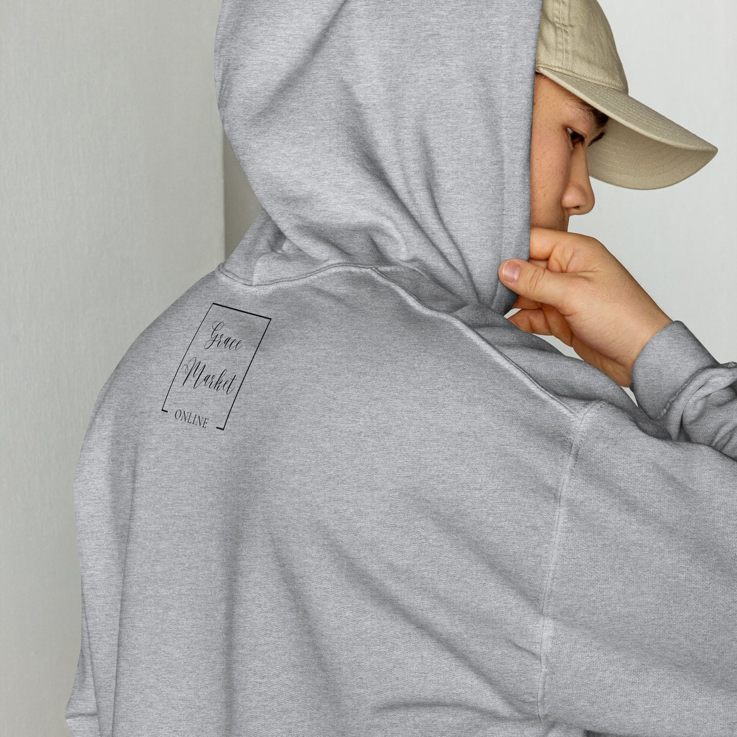 A person turned almost backwards so you can see they are wearing a ball cap, but they have on a light gray sweatshirt with a hood and they have lifted the hood up onto their head and you can see the brand on the back of the sweatshirt printed:  Grace Market Online.