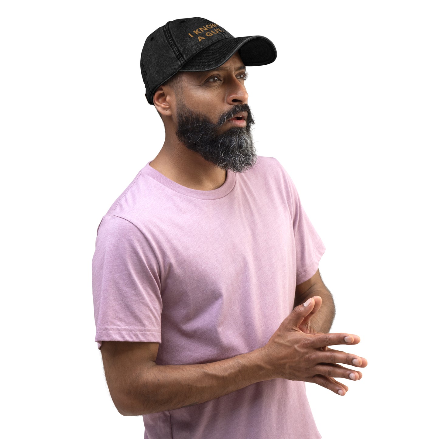 Bearded man in pink t-shirt on a plain white background wearing a black baseball cap with words embroidered on it.