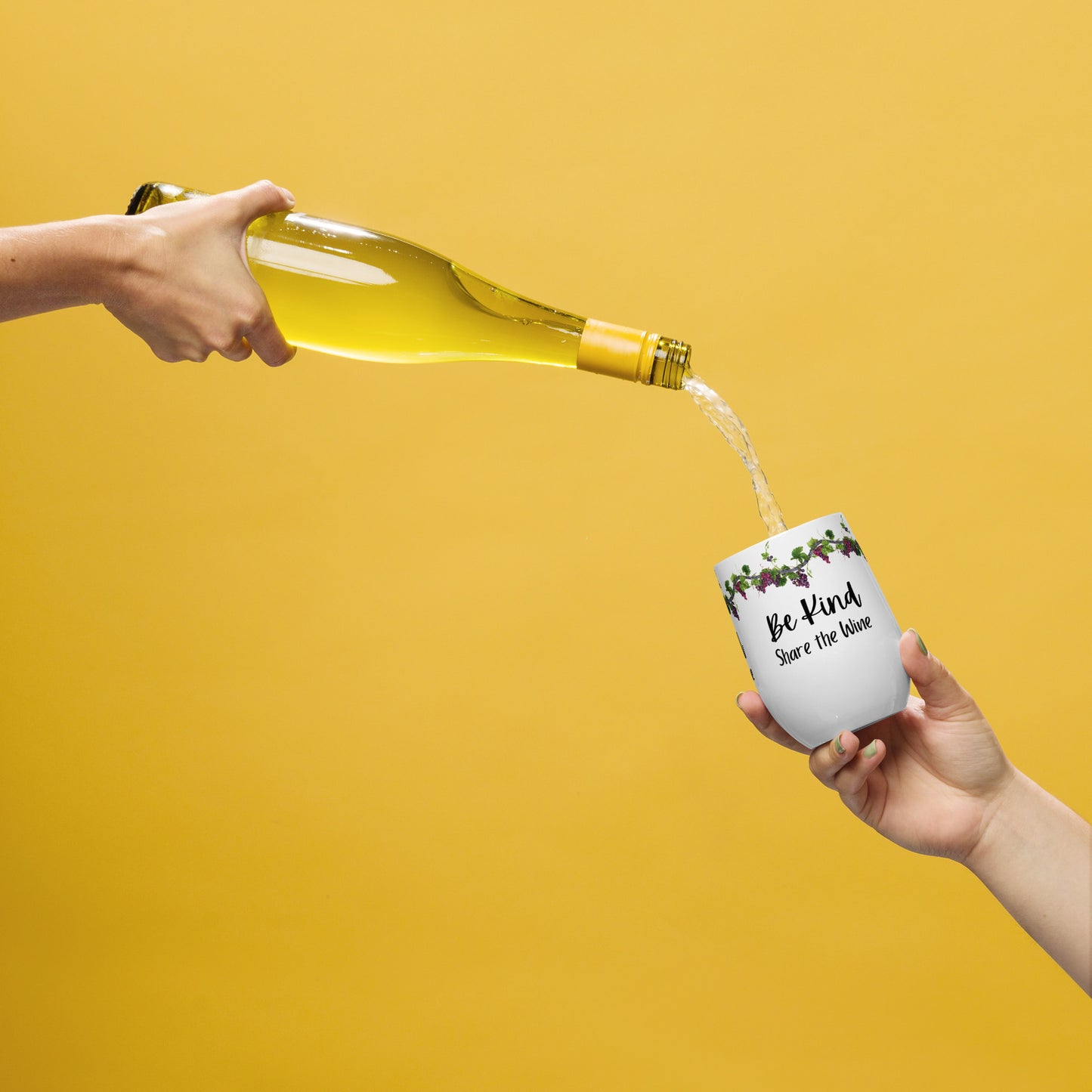 A yellowish gold background and on the left side there is a hand holding a wine bottle with wine pouring out of it into a wine tumbler being held by a hand on the right side and the wine tumbler says Be Kind Share the Wine and has grapes and grapevines along the top of it.