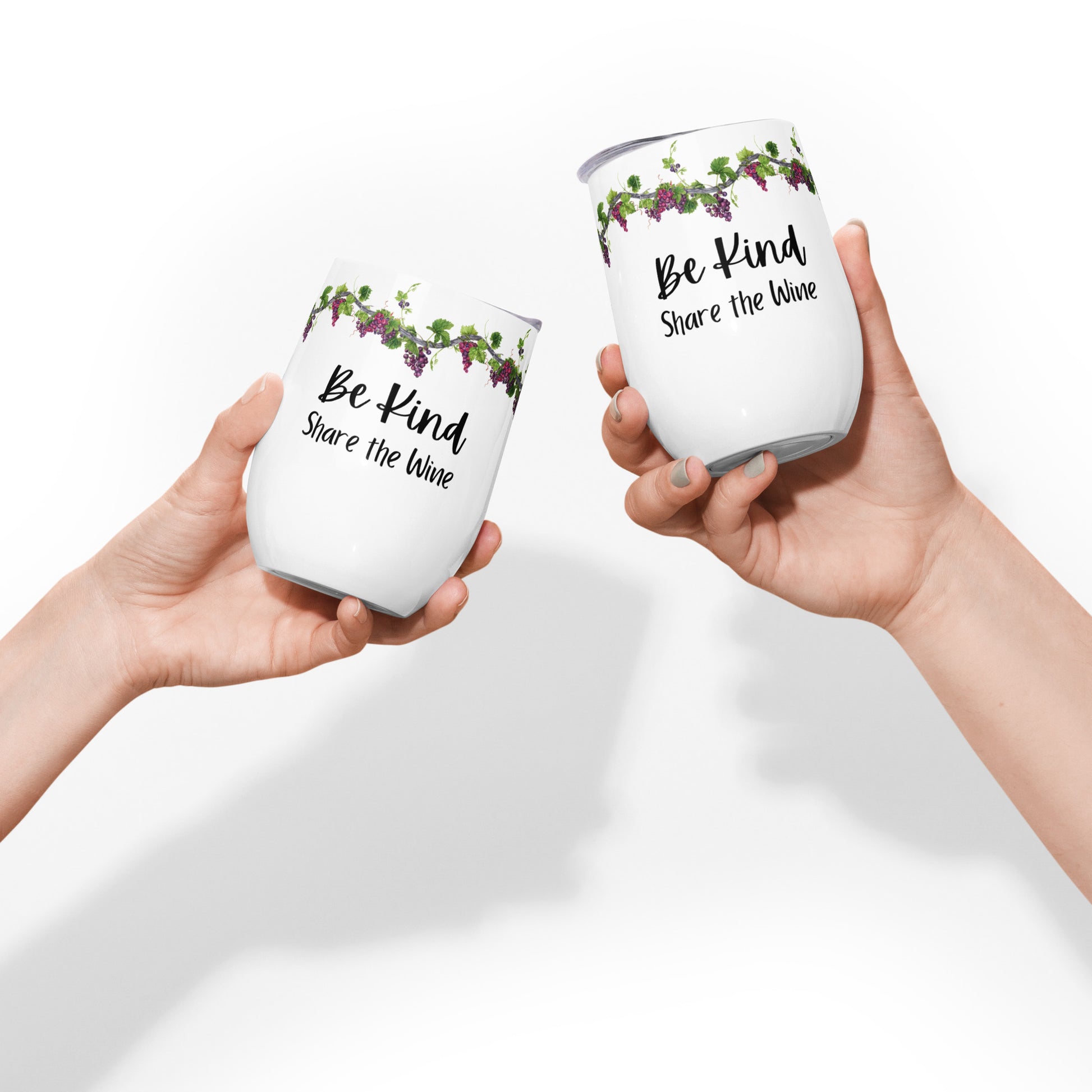 Two woman's manicured hands are shown with two identical stainless steel wine tumblers, one in each hand, that are white and say "Be Kind Share the Wine" with a row of grapevines with purple grapes along the top edge, tilted like they were clinking them together to say Cheers, on a solid white background.