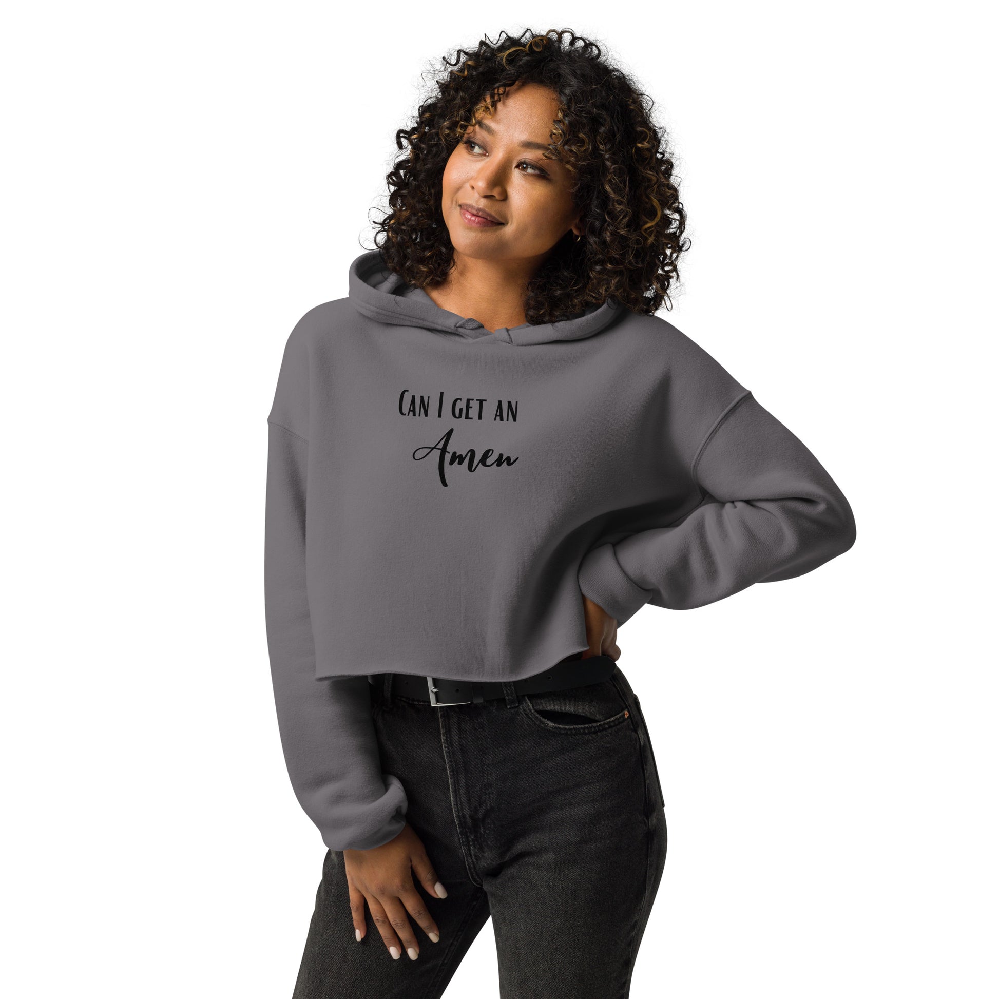 Can I Get an Amen is printed in two different fonts on the front of a medium gray cropped hooded sweatshirt with long sleeves, worn  by a smiling woman with curly hair, over belted black jeans.