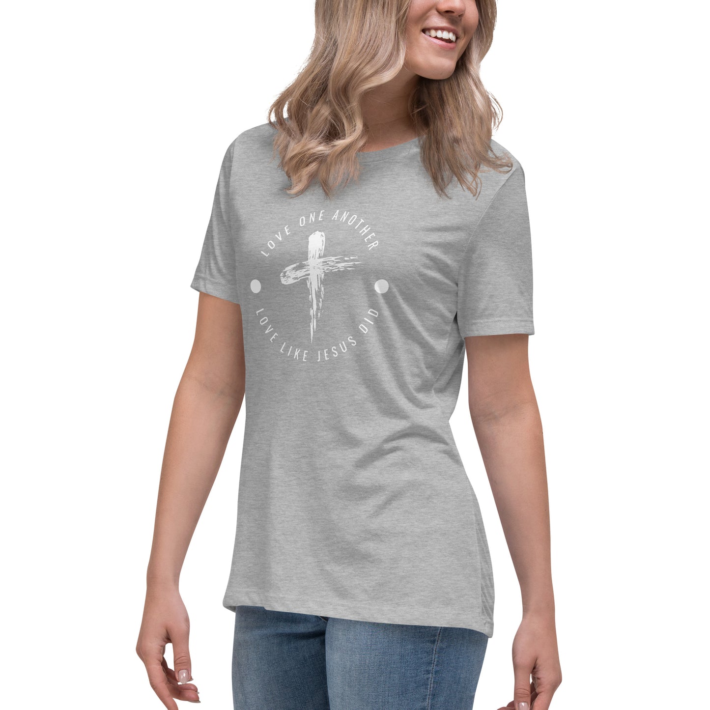 A partial view of a woman wearing a light gray or ash colored short-sleeved t-shirt with a circle kind of emblem where the words Love One Another Love Like Jesus Did are in a circle with a cross graphic in the center.