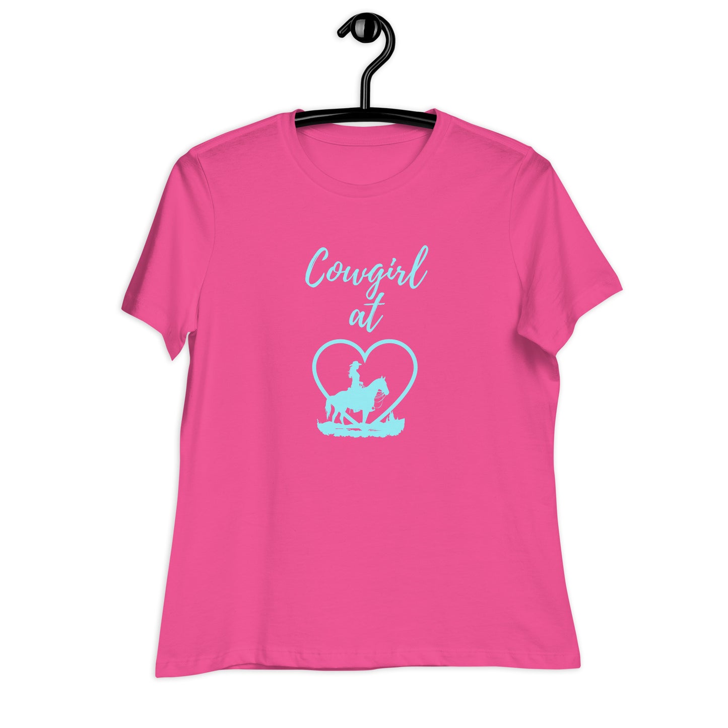 Bright pink t-shirt on a black hanger against a bright white background and the t-shirt has an aqua cowgirl and heart design above which it says "Cowgirl at" ... meaning "Cowgirl at Heart"