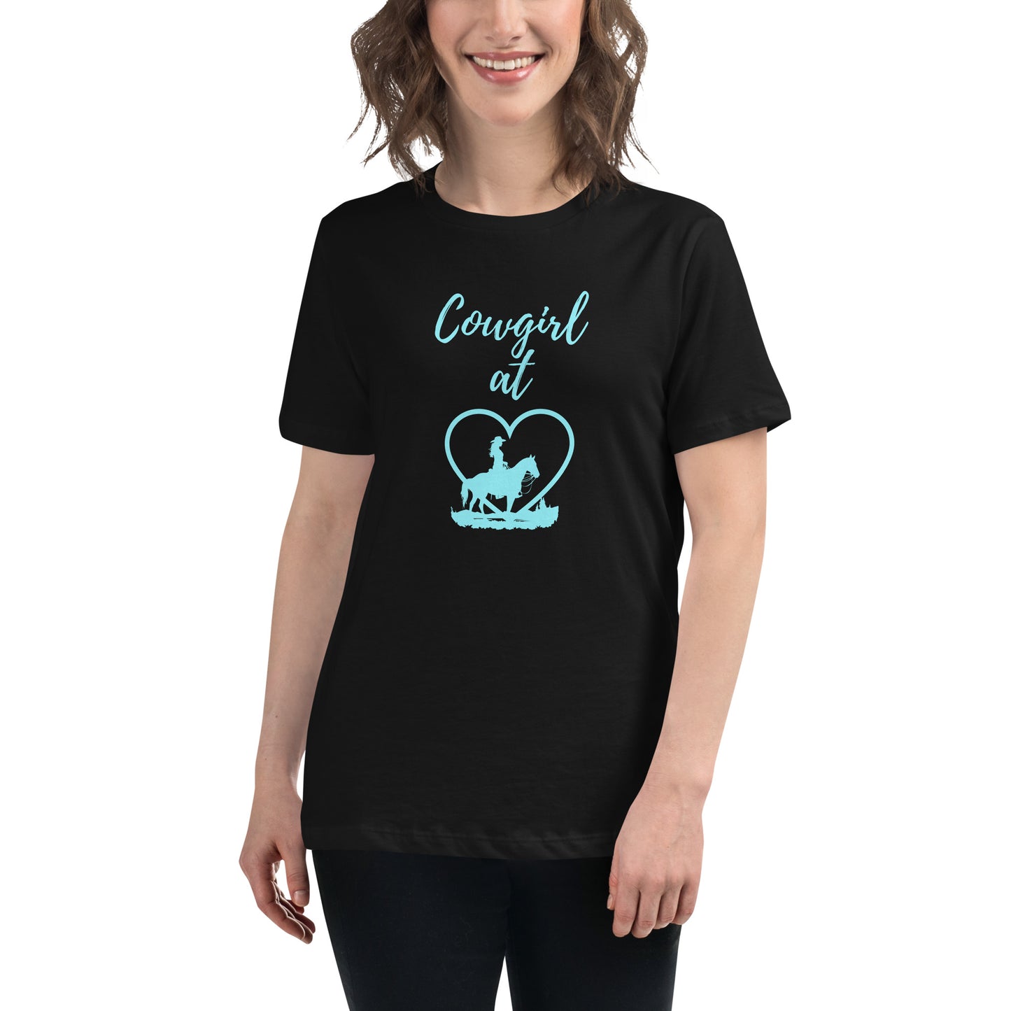 A partial view of a woman with wavy shoulder length hair wearing dark pants and a black t-shirt with an aqua design on the front that says Cowgirl at in script and then a heart with a profile view of a horse and a cowgirl on his back standing in front of the heart.