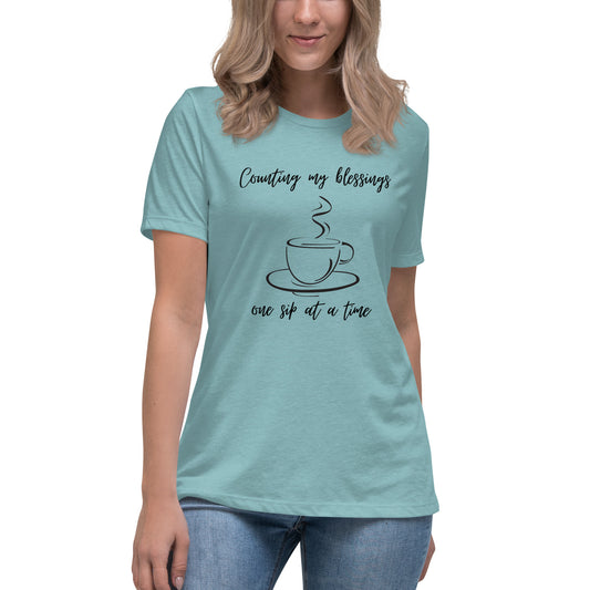 Blond woman wearing aqua/teal short-sleeved t-shirt with a steaming coffee up in the middle and the words:  Counting my blessings one sip at a time.