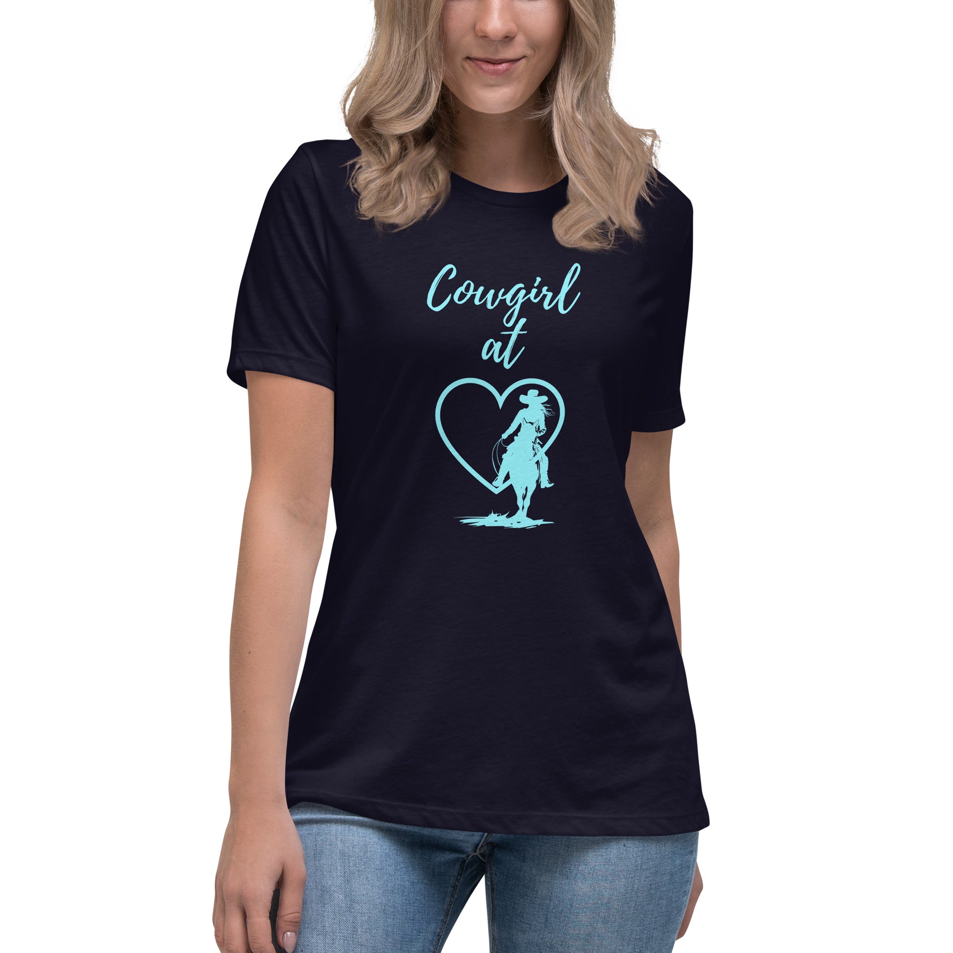 A view of a woman from about her nose to her thighs with long blonde hair and she is wearing a navy short-sleeved t-shirt with an aqua design on the front that has a silhouette of a cowgirl on a horse in front of a heart so that it says Cowgirl at and then the heart.