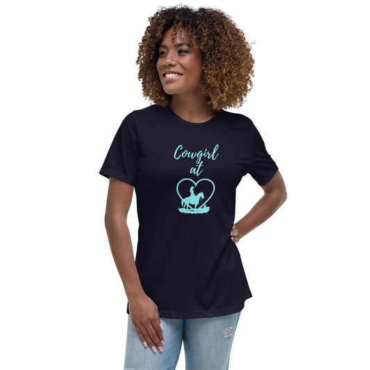 A woman with dark curly shoulder-length hair stands with one hand on hip, wearing light denim jeans and a navy short-sleeved t-shirt with an aqua design that says Cowgirl at and then a heart and a profile silhouette of a girl on horseback with a cowboy hat.