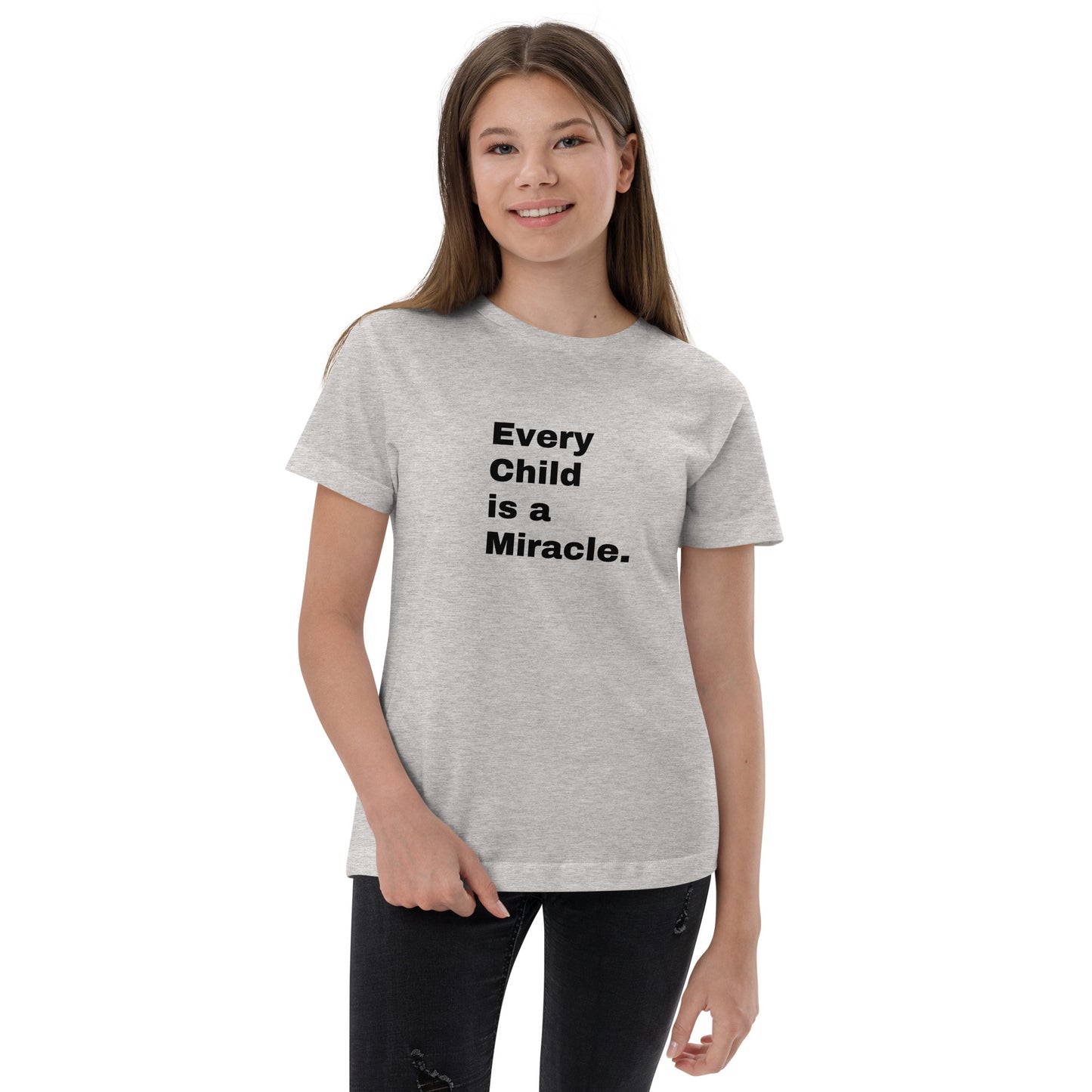 Young teenaged girl with long hair wears dark pants and a light gray short sleeve t-shirt that says "Every Child is a Miracle." in black text.