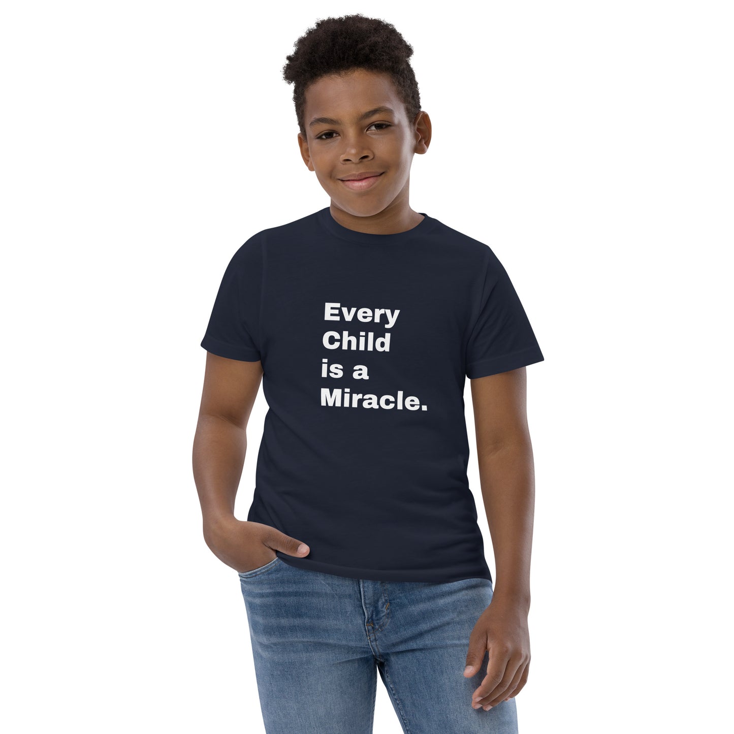 Smiling boy with short black hair is wearing jeans and a short-sleeve black or dark navy t-shirt with white text on the front saying:  "Every Child is a Miracle."